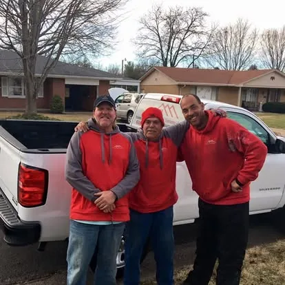 Three crew members in red H&H shirts beside a white pickup