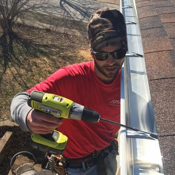 An H&H worker fastening a white gutter along a shingle roof